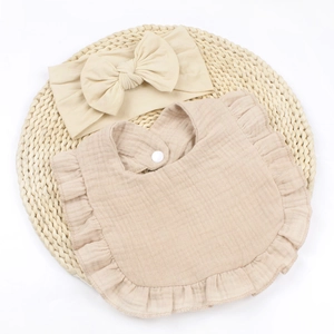 Detail of soft muslin baby bib with ruffles and matching bow headband in beige