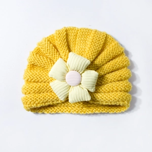 Detail view of yellow baby knitted hat with a large decorative fabric flower on white background