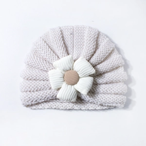 Detailed view of cream baby knitted turban hat with white floral ornament and brown center