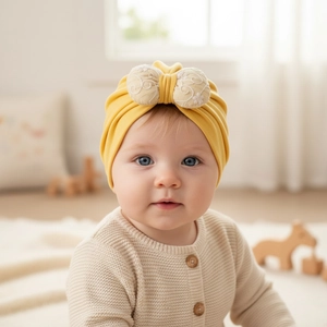 Detail of baby turban hat in yellow with a large beige embroidered floral bow