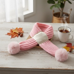 Pink knit baby scarf with soft pom poms and cream buckle on a cozy autumn wooden table