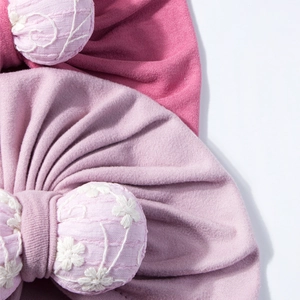 Close-up of baby turbans with 3D bows and white floral embroidery in pink and purple colors