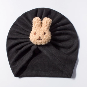 Detail view of the black baby turban hat featuring a beige plush rabbit and pleated texture