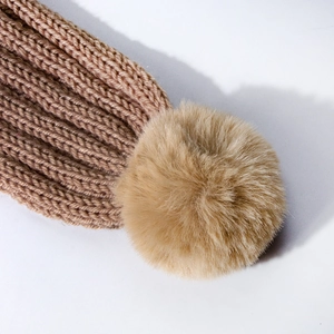 Detailed macro view of the warm brown ribbed knit texture and fluffy pom-pom detail