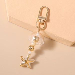 Détail du pendentif étoile de mer dorée et breloque muguet avec perles blanches