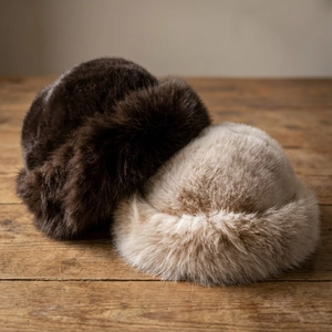 Plush faux fur winter mongolian hats in dark brown and beige on a vintage wood surface