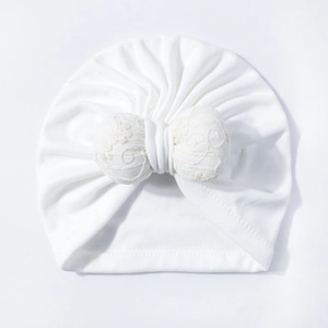Close-up of white baby turban with detailed lace embroidery on a large bow detail