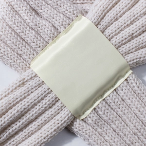 Macro detail of cream knit baby scarf with vertical texture and satin patch detail