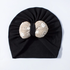 Detail of baby turban hat with a beige bow featuring floral embroidery and vine patterns