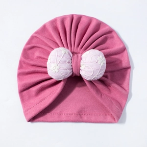 Detail of baby turban hat featuring pink floral lace bow and pleated cotton fabric