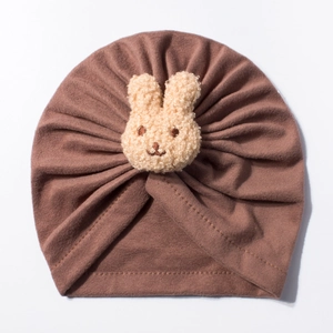 Detail of dark brown knitted baby turban hat with a plush 3D bunny doll decoration