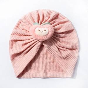 Detailed view of pink waffle knit baby turban hat with a cute 3D plush peach doll decoration