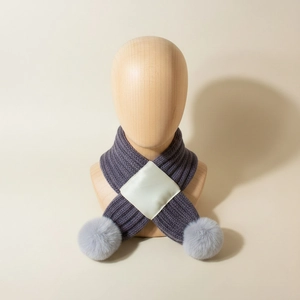 Detailed knit texture of purple baby scarf featuring soft grey faux fur pom-poms