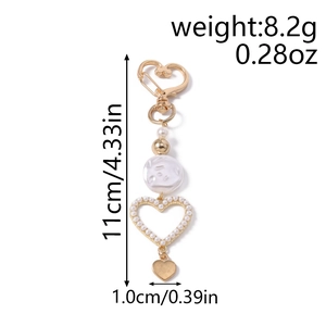 Detail of heart-shaped pearl bag charm with golden lobster clasp and white textured beads