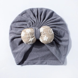 Close-up of grey baby turban hat with beige stuffed bow and white floral embroidery