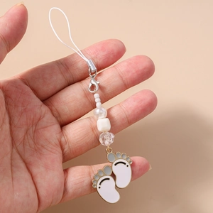 Close-up of white enamel paw pendant and beaded strap held in hand for phone accessory detail