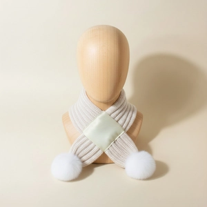 Detail of baby ribbed knit scarf with cross design and soft plush white pom-poms
