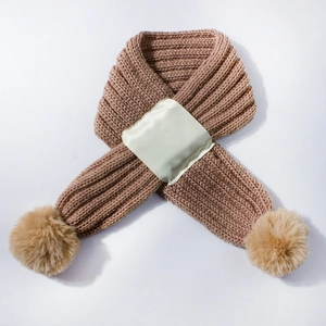 Detail of warm khaki knit baby scarf featuring thick texture and large soft pom-poms