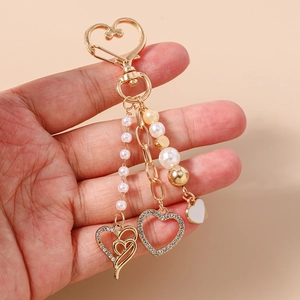 Détail d'un porte-clés doré en cœur avec perles blanches et charmes en strass brillants