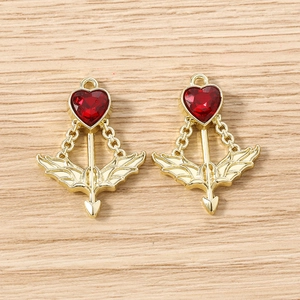 Detailed view of Cupid's arrow pendants with red heart stones on wood background