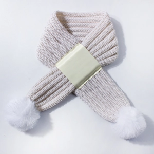 Close-up of cream chunky knit baby scarf with white faux fur pom poms and cross-over strap