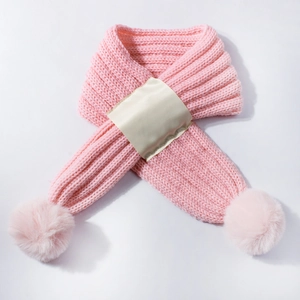 Detailed view of pink knitted baby scarf with fluffy pom-poms and blank satin label