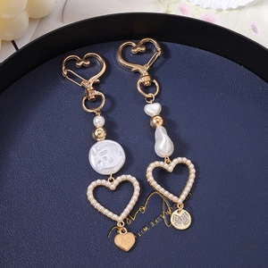 Close-up of pearl heart keychain pendants with gold accents on a deep blue tray