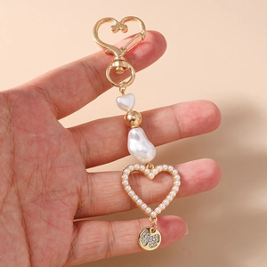 Close-up of heart pearl keychain with gold clover pendant held by a hand on beige background