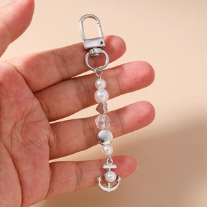Détail d'un porte-clés en perles avec pendentif ancre argenté tenu dans la main