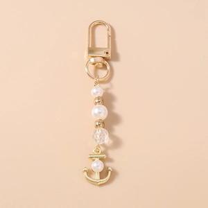 Détail d'un porte-clés ancre marine avec perles blanches et perles dorées sur fond clair