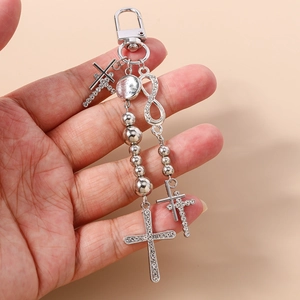 Detailed view of silver cross keychain with rhinestones and beads held in hand