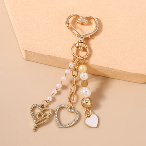 Vue détaillée du porte-clés cœur doré avec perles, strass et breloques en émail blanc