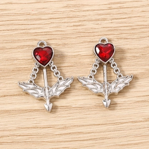 Macro detail of silver Cupid arrow charms with faceted red heart gemstone for DIY jewelry
