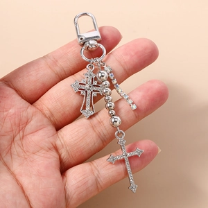 Detailed view of silver cross keychain charms with rhinestones held in hand