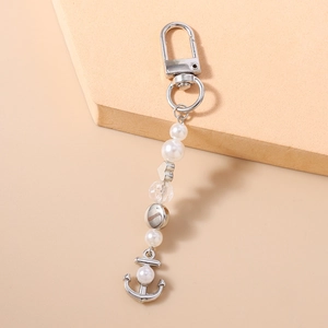 Détail du porte-clés ancre argenté avec perles blanches et cristal sur support beige