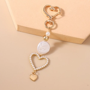 Detail of a heart-shaped pearl keychain with golden clasp on a minimalist display
