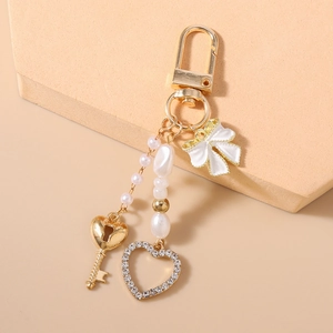 Detail eines goldfarbenen Perlen-Schlüsselanhängers mit Schleife, Herz und Strass