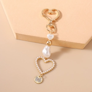 Detail view of heart-shaped pearl bag charm with golden carabiner and crystal pendant