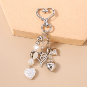 Détail du porte-clés coeur perlé avec pendentifs en alliage argenté sur présentoir beige