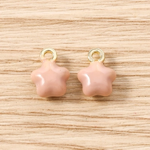 Détail macro de deux pendentifs étoiles en émail rose clair avec anneaux en métal doré