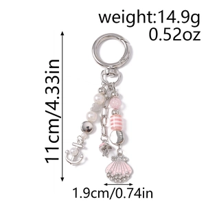 Detail view of a pearl keychain with pink enamel scallop and anchor charms on white background