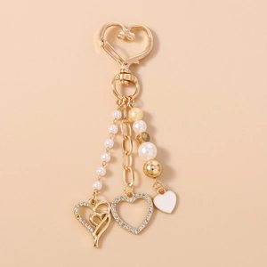 Détail d'un porte-clés cœur doré avec cristaux brillants, perles blanches et breloques