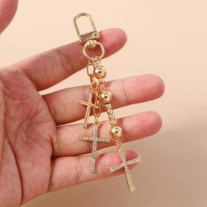 Handheld view of gold cross keychain with rhinestones and polished bead details