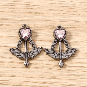 Macro shot of gun-black heart arrow pendants with pink gemstone on wood surface