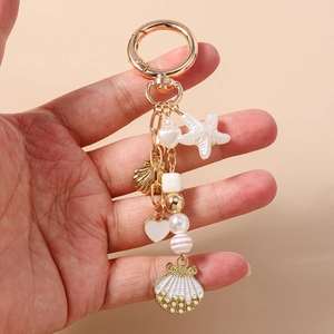 Detail of nautical keychain with gold starfish, white shell and pearl charms held in hand