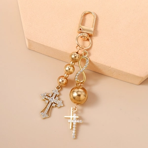 Close-up of golden beaded keychain with rhinestone cross and infinity symbol charm