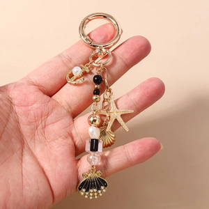 Detail view of gold starfish, seashell, and pearl anchor charms on a beaded keychain