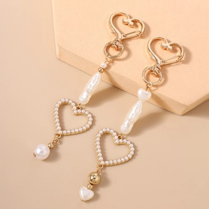 Fashionable gold beaded keychain with hollow heart charm and baroque pearls on beige background