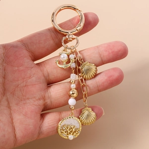 Détail d'un porte-clés doré avec ancre, perle, coquillages et breloques corail à la main