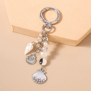 Close-up of ocean-themed keychain with shell, anchor, and pearl charms on a beige pedestal